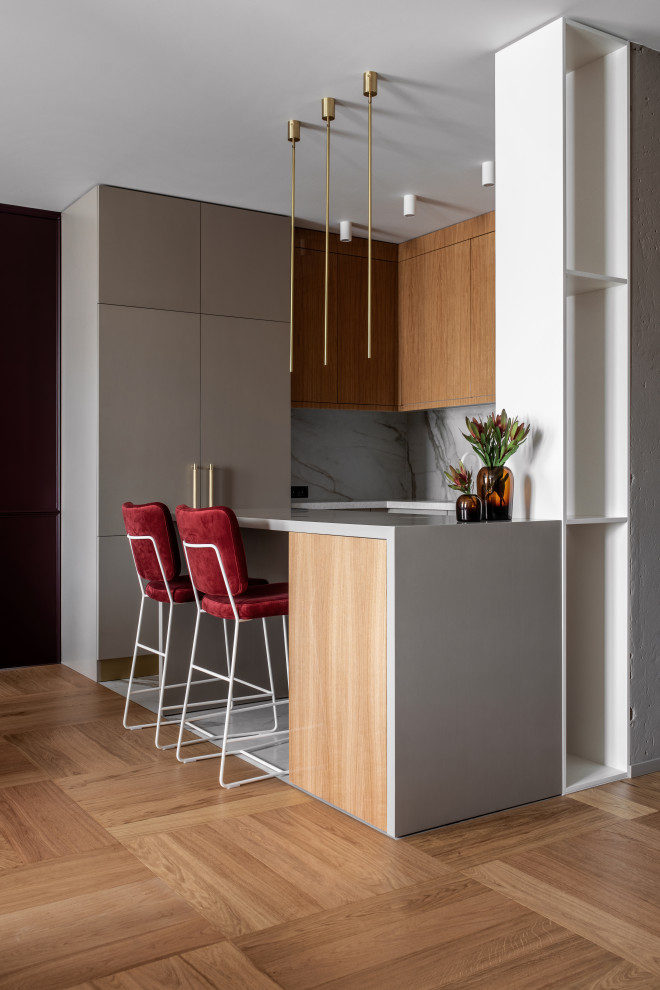 Small contemporary l-shaped kitchen in Other with flat-panel cabinets, grey cabinets, grey splashback, integrated appliances, light hardwood flooring, a breakfast bar, beige floors and grey worktops.