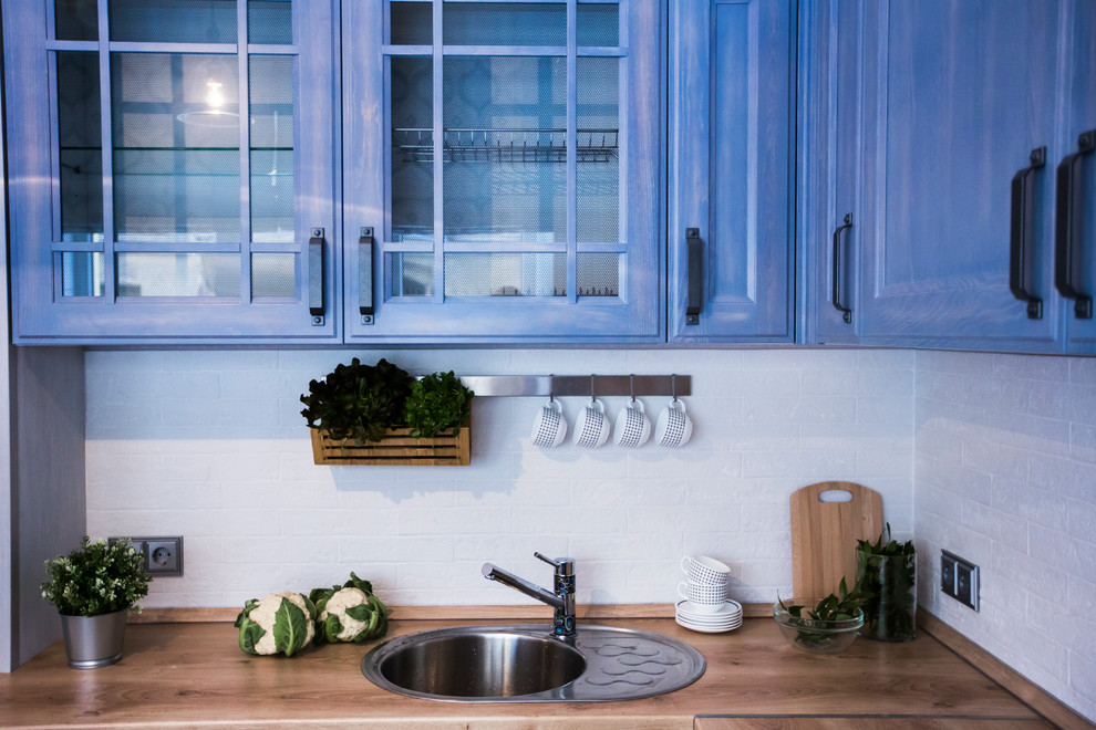 Inredning av ett industriellt kök, med en nedsänkt diskho, luckor med infälld panel, blå skåp, laminatbänkskiva, vitt stänkskydd, stänkskydd i tegel, svarta vitvaror, klinkergolv i porslin och beiget golv