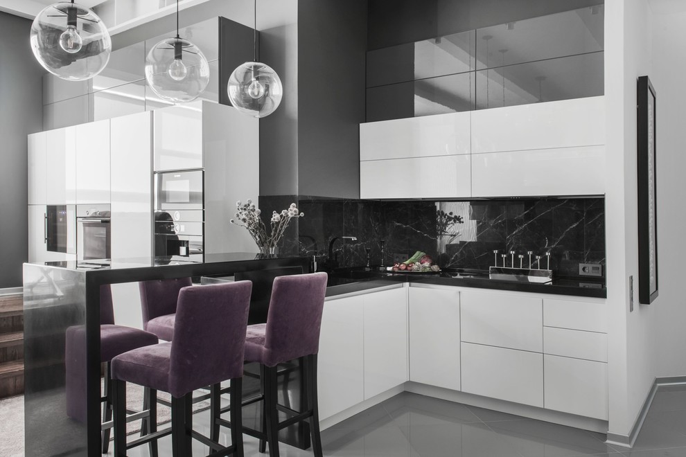 Стильный дизайн: угловая кухня-гостиная в современном стиле с плоскими фасадами, белыми фасадами, черным фартуком, полуостровом, серым полом и техникой из нержавеющей стали - последний тренд
