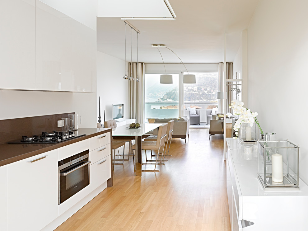 Immagine di una cucina minimal di medie dimensioni con ante lisce, ante bianche, elettrodomestici neri, parquet chiaro e top in superficie solida