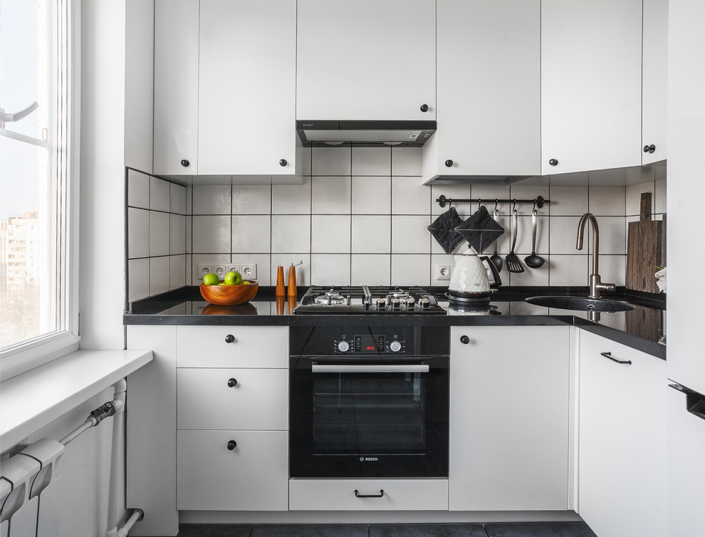 Источник вдохновения для домашнего уюта: угловая, отдельная кухня в скандинавском стиле с плоскими фасадами, белым фартуком, врезной мойкой, черной техникой, черным полом, черно-белыми фасадами и мойкой в углу без острова