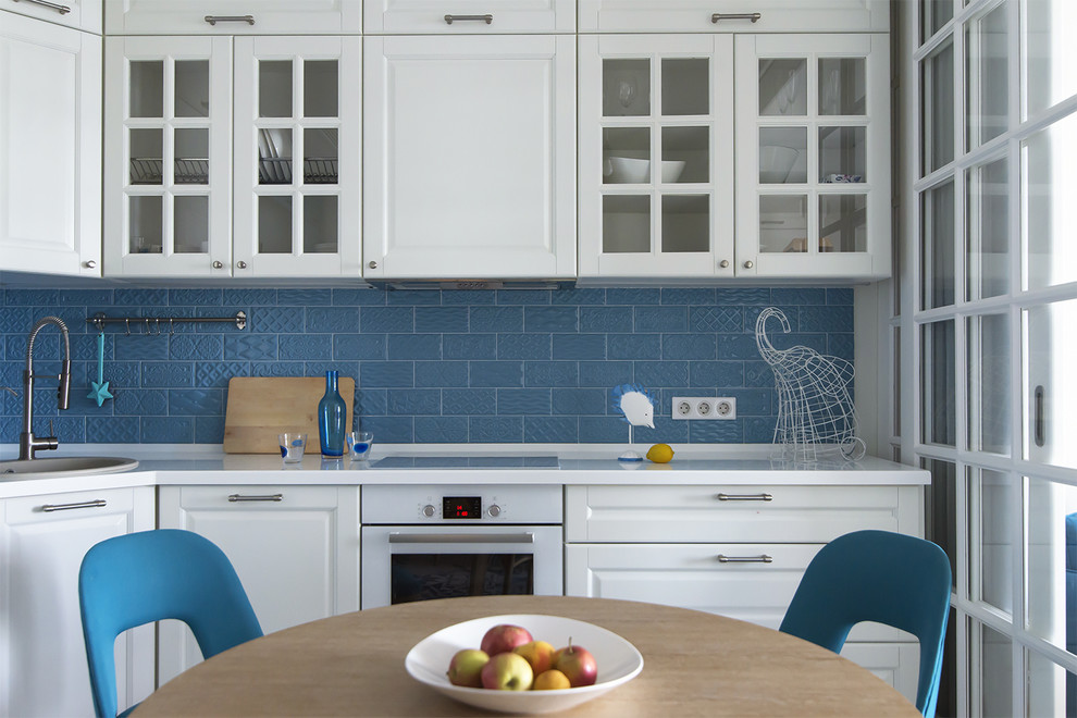 Пример оригинального дизайна: маленькая угловая кухня-гостиная в современном стиле с фасадами с выступающей филенкой, белыми фасадами, столешницей из акрилового камня, синим фартуком, фартуком из керамической плитки, белой техникой, полом из керамической плитки, синим полом и накладной мойкой без острова для на участке и в саду