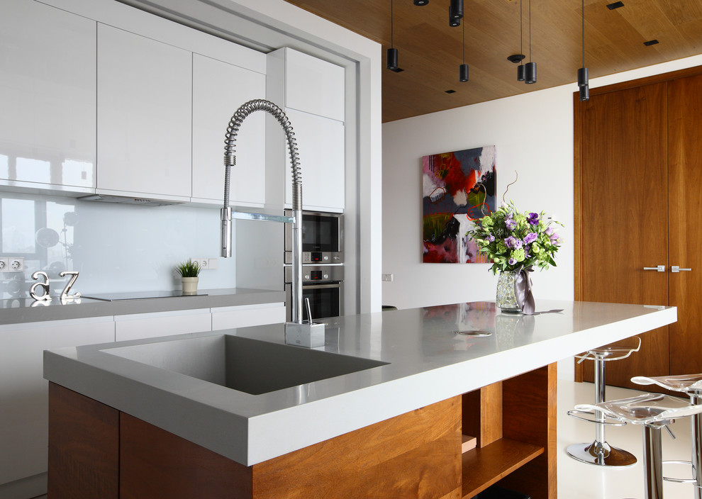 Bild på ett mellanstort funkis kök, med släta luckor, vita skåp, bänkskiva i kvartsit, vitt stänkskydd, glaspanel som stänkskydd, rostfria vitvaror, en köksö och en integrerad diskho