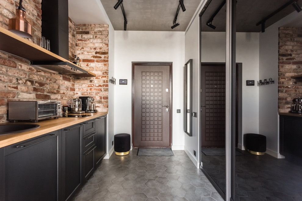 Cette photo montre une cuisine linéaire industrielle avec un évier posé, un placard avec porte à panneau encastré, des portes de placard noires, une crédence marron, une crédence en brique, un sol gris et un plan de travail marron.