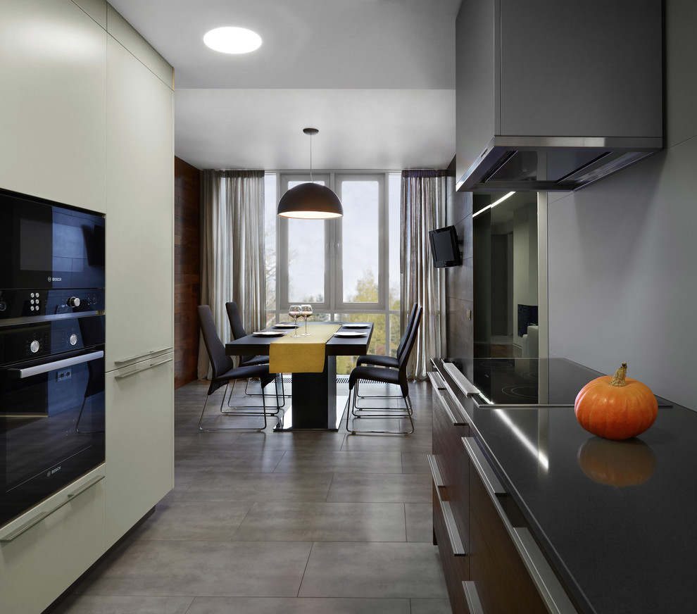 Modelo de cocina actual abierta con armarios con paneles lisos, puertas de armario de madera en tonos medios, salpicadero verde y electrodomésticos negros