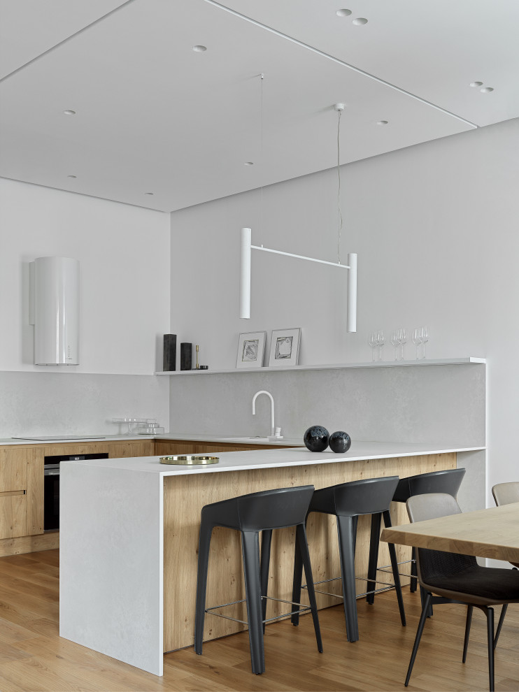 Exemple d'une cuisine tendance en U et bois clair avec un placard à porte plane, une crédence blanche, un électroménager noir et un plan de travail blanc.