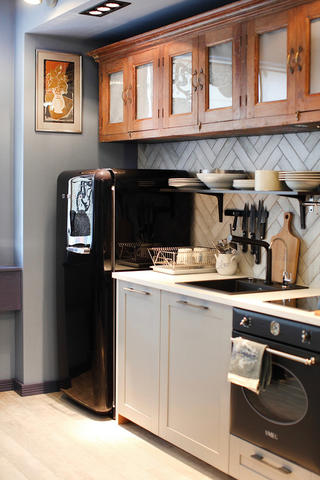 На фото: маленькая прямая кухня-гостиная в стиле фьюжн с накладной мойкой, серыми фасадами, серым фартуком, черной техникой и светлым паркетным полом для на участке и в саду с