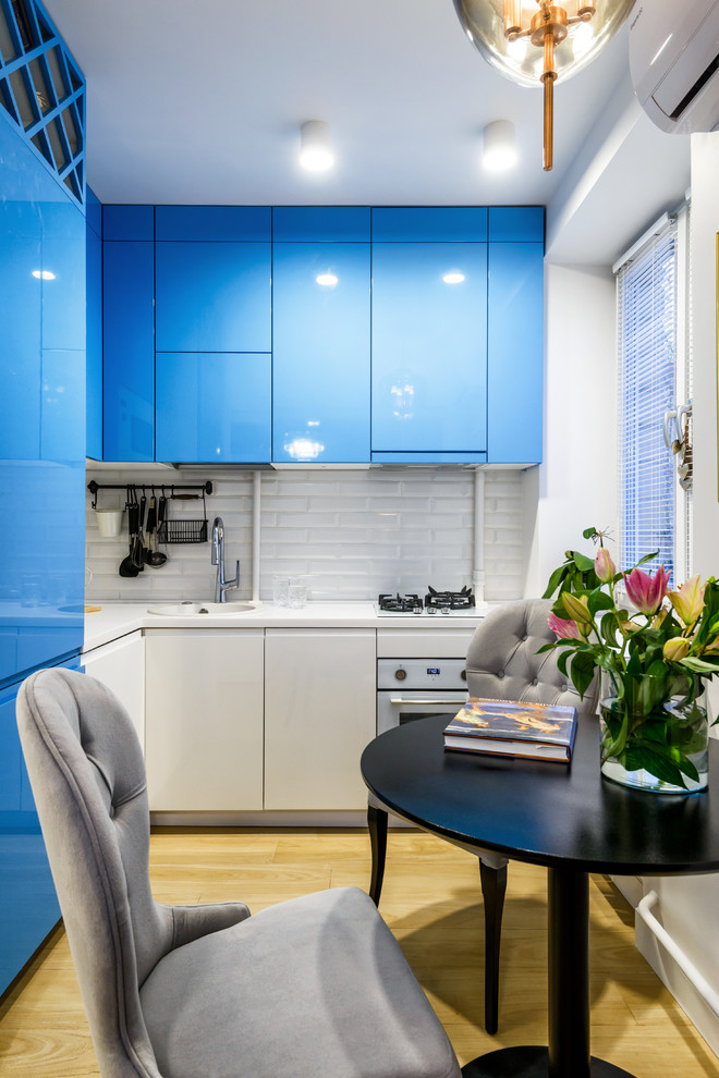 Moderne Küche ohne Insel in L-Form mit flächenbündigen Schrankfronten, blauen Schränken, Küchenrückwand in Weiß, Rückwand aus Metrofliesen, weißen Elektrogeräten, hellem Holzboden und beigem Boden in Moskau