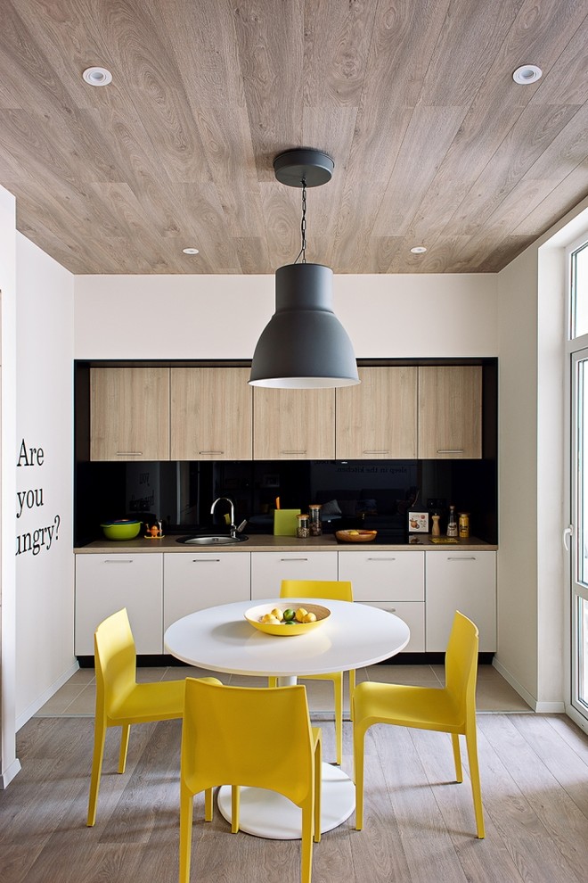 Пример оригинального дизайна: прямая кухня в скандинавском стиле с обеденным столом, накладной мойкой, черным фартуком и светлым паркетным полом без острова