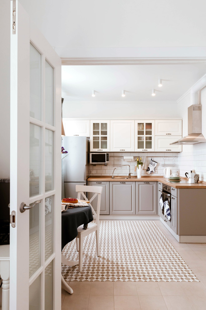 Scandi l-shaped kitchen/diner in Other with a built-in sink, raised-panel cabinets, beige cabinets, wood worktops, white splashback, metro tiled splashback, stainless steel appliances, no island, multi-coloured floors and brown worktops.