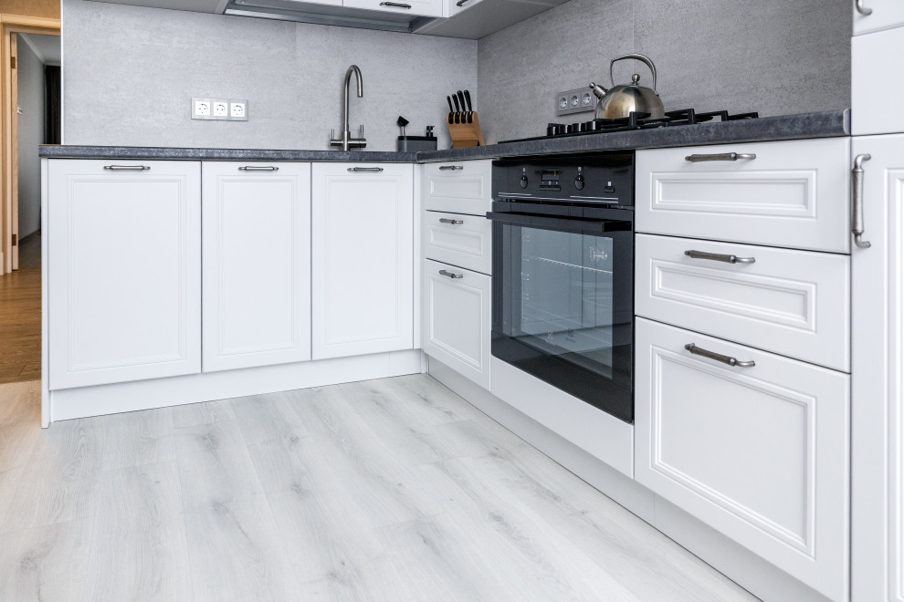 Idee per una cucina nordica di medie dimensioni con ante con riquadro incassato, ante bianche, top in laminato, elettrodomestici neri, pavimento in laminato, pavimento grigio e top grigio