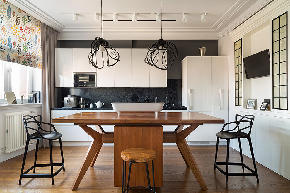 Bild på ett funkis linjärt kök och matrum, med en köksö, släta luckor, vita skåp, svart stänkskydd, brunt golv, en undermonterad diskho, träbänkskiva, integrerade vitvaror och mellanmörkt trägolv