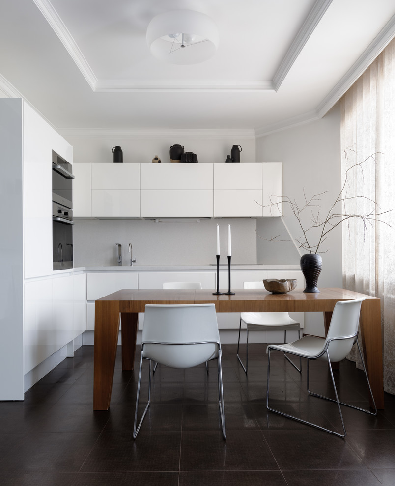 На фото: угловая, светлая кухня в современном стиле с обеденным столом, плоскими фасадами, белыми фасадами и черной техникой