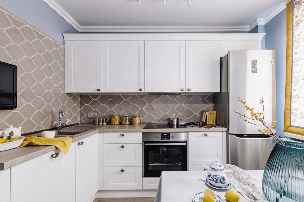 Small scandi l-shaped kitchen/diner in Other with a built-in sink, recessed-panel cabinets, white cabinets, laminate countertops, grey splashback, ceramic splashback, stainless steel appliances, laminate floors, no island, grey floors and grey worktops.