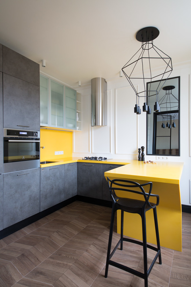 Idéer för att renovera ett funkis gul gult u-kök, med en undermonterad diskho, släta luckor, grå skåp, gult stänkskydd, rostfria vitvaror, mörkt trägolv, en halv köksö och brunt golv