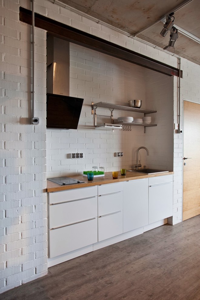 Свежая идея для дизайна: прямая кухня-гостиная в современном стиле с накладной мойкой, плоскими фасадами, белыми фасадами, белым фартуком и фартуком из кирпича без острова - отличное фото интерьера