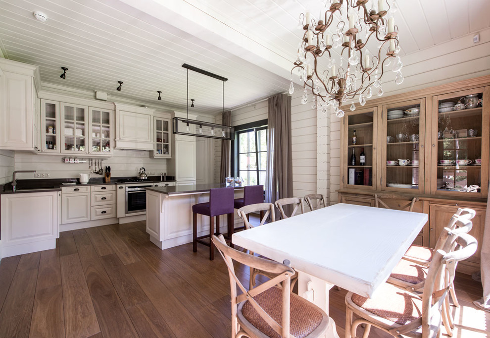 Diseño de cocina campestre con puertas de armario blancas, salpicadero blanco, electrodomésticos de acero inoxidable, suelo de madera en tonos medios y una isla