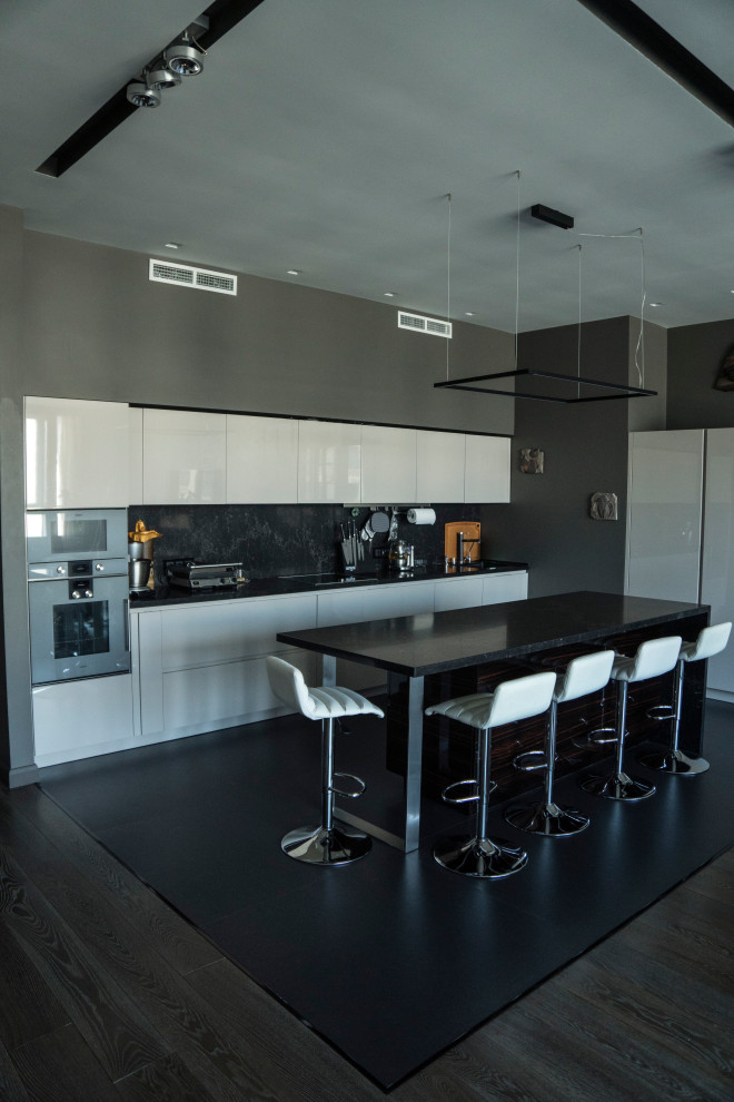 Immagine di una cucina minimal di medie dimensioni con lavello sottopiano, ante lisce, ante bianche, top in granito, paraspruzzi nero, elettrodomestici bianchi, pavimento in gres porcellanato, pavimento grigio e top nero