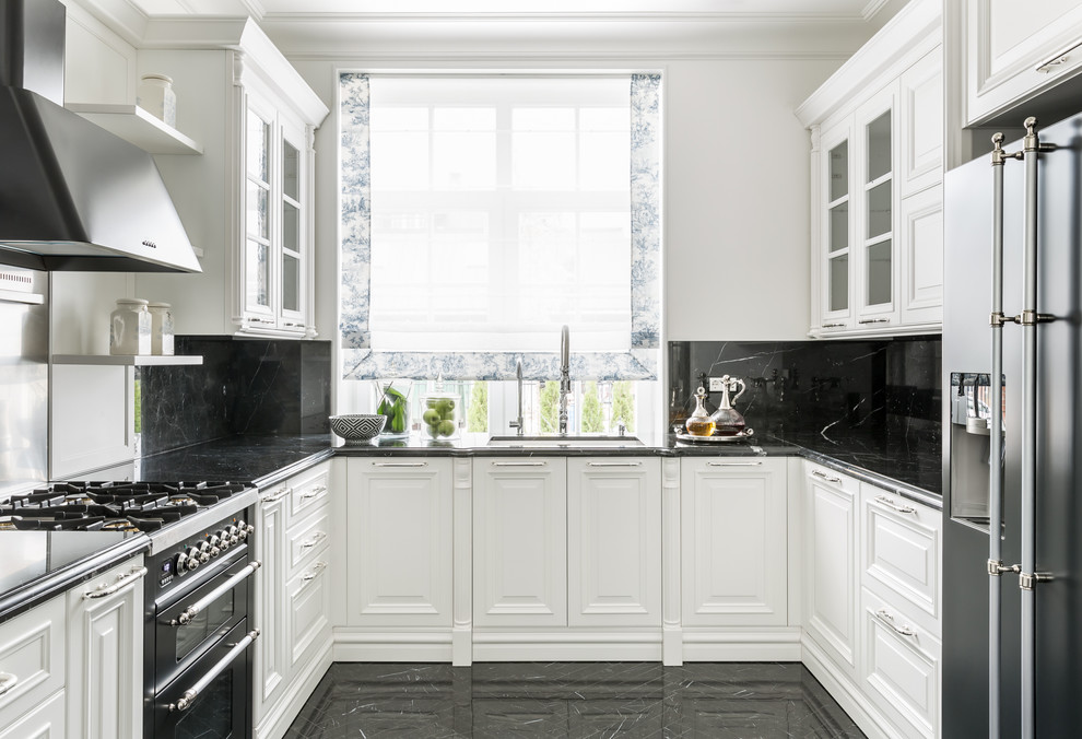 Photo of a classic u-shaped kitchen in Other with a submerged sink, raised-panel cabinets, white cabinets, black splashback, stone slab splashback, stainless steel appliances, black floors and black worktops.