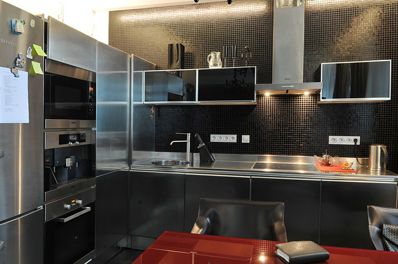 Mid-sized trendy l-shaped porcelain tile eat-in kitchen photo in Moscow with a drop-in sink, flat-panel cabinets, stainless steel cabinets, stainless steel countertops, black backsplash, mosaic tile backsplash, black appliances and no island