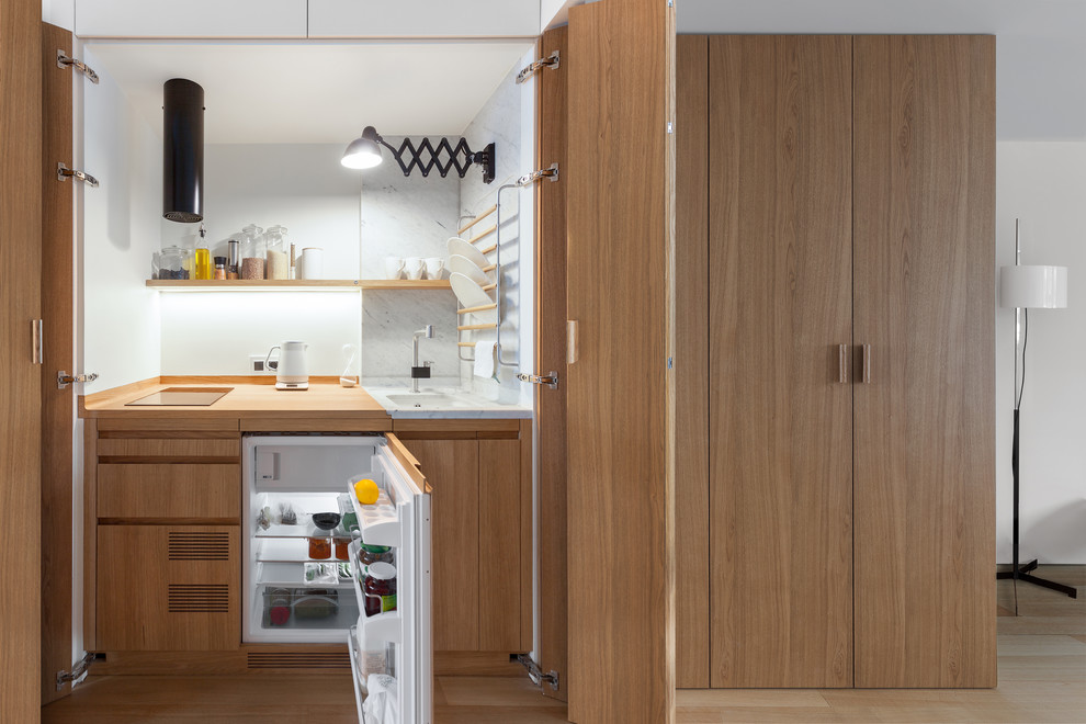 Photo of a small contemporary enclosed kitchen in Moscow with a submerged sink, medium wood cabinets, wood worktops, white splashback, integrated appliances and medium hardwood flooring.