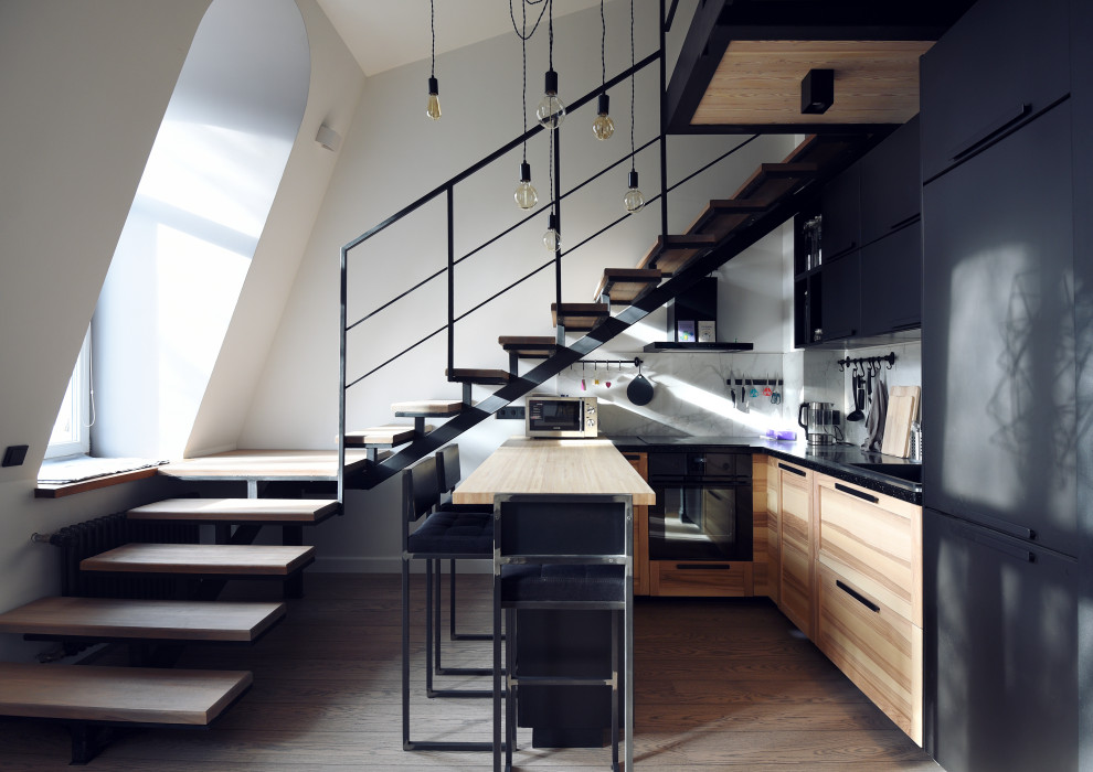 Inspiration for a small urban u-shaped kitchen in Saint Petersburg with an integrated sink, flat-panel cabinets, light wood cabinets, black appliances, medium hardwood flooring, a breakfast bar, brown floors and beige worktops.