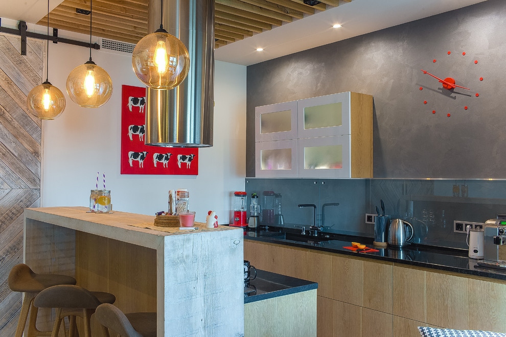 На фото: прямая кухня-гостиная в стиле фьюжн с плоскими фасадами, светлыми деревянными фасадами, серым фартуком, фартуком из стекла, монолитной мойкой и полуостровом с
