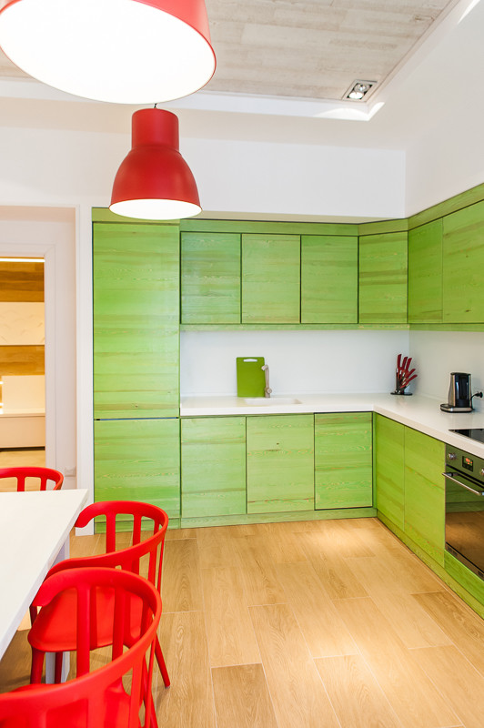 Imagen de cocina contemporánea sin isla con armarios con paneles lisos, puertas de armario verdes, salpicadero blanco, electrodomésticos negros, suelo marrón y encimeras blancas