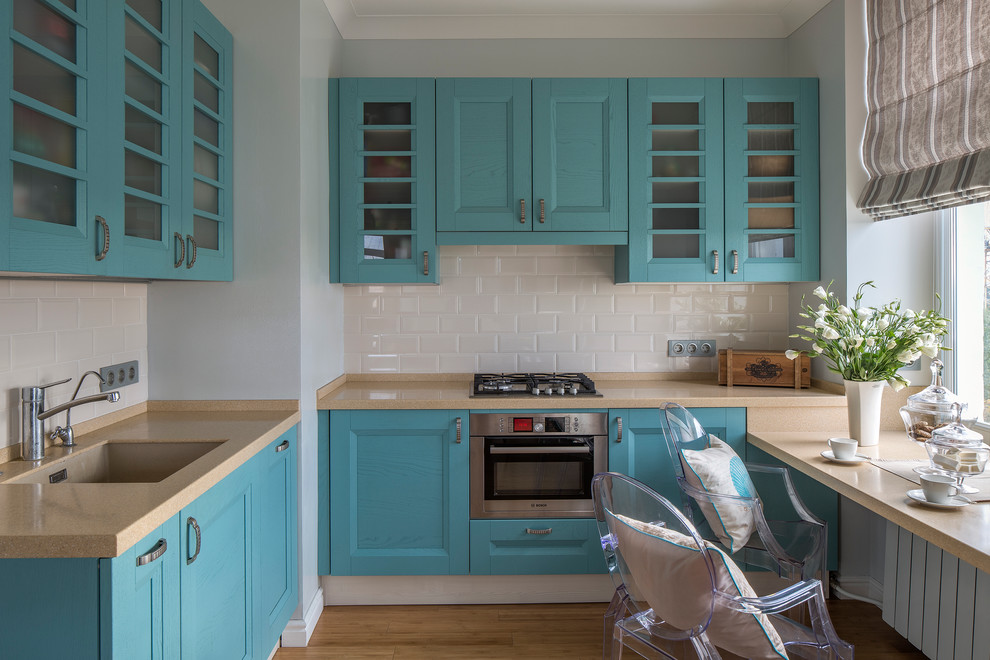 Exempel på ett klassiskt l-kök, med en undermonterad diskho, luckor med infälld panel, blå skåp, vitt stänkskydd, stänkskydd i tunnelbanekakel, rostfria vitvaror och mellanmörkt trägolv
