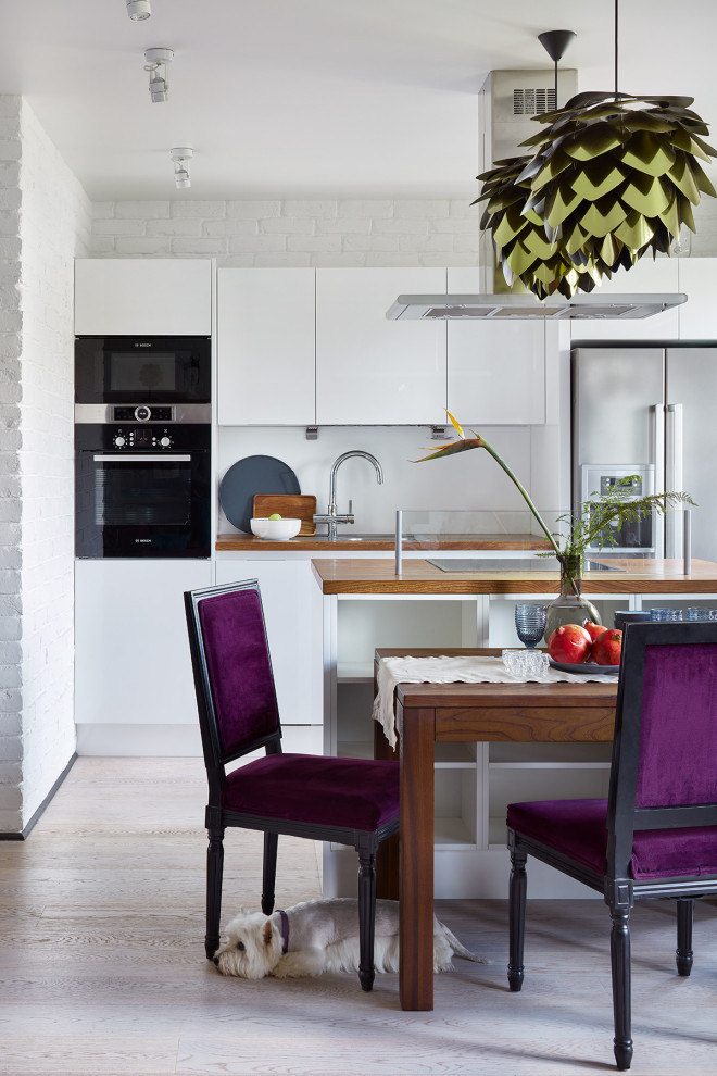 Example of a mid-sized trendy galley beige floor eat-in kitchen design in Moscow with a drop-in sink, flat-panel cabinets, white cabinets, wood countertops, white backsplash, stainless steel appliances, an island and brown countertops