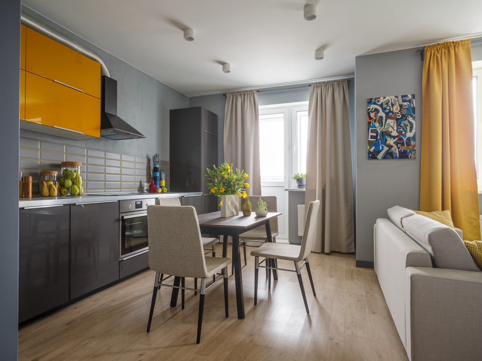 This is an example of a contemporary single-wall open plan kitchen in Moscow with flat-panel cabinets, yellow cabinets, grey splashback, stainless steel appliances, light hardwood flooring, no island and beige floors.
