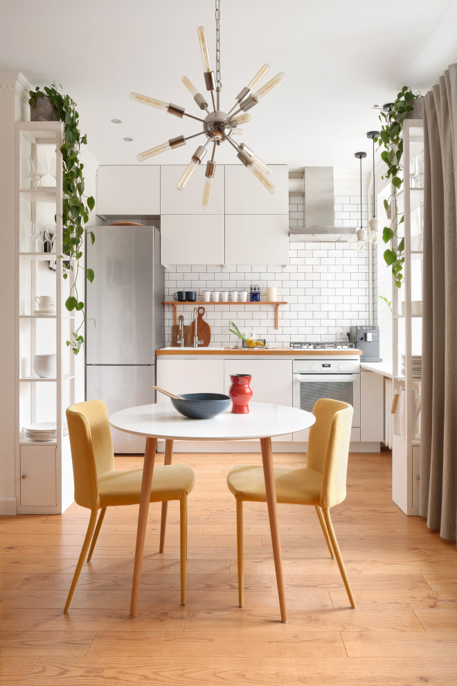 Scandi l-shaped kitchen/diner in Moscow with a built-in sink, flat-panel cabinets, white cabinets, wood worktops, white splashback, medium hardwood flooring, no island, brown floors, brown worktops and white appliances.