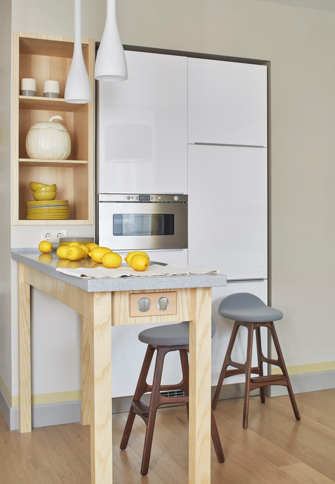 Ejemplo de cocina lineal contemporánea abierta con armarios con paneles lisos, puertas de armario blancas, electrodomésticos de acero inoxidable, suelo de madera clara y barras de cocina