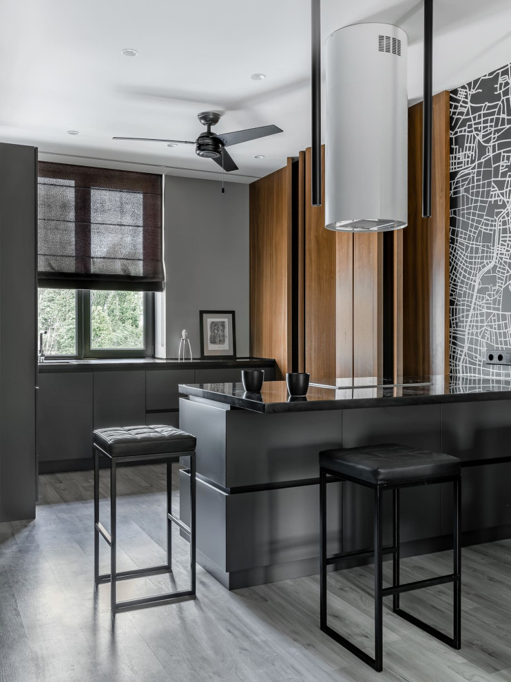 This is an example of a contemporary galley open plan kitchen in Other with flat-panel cabinets, grey cabinets, a breakfast bar, grey floors and black worktops.