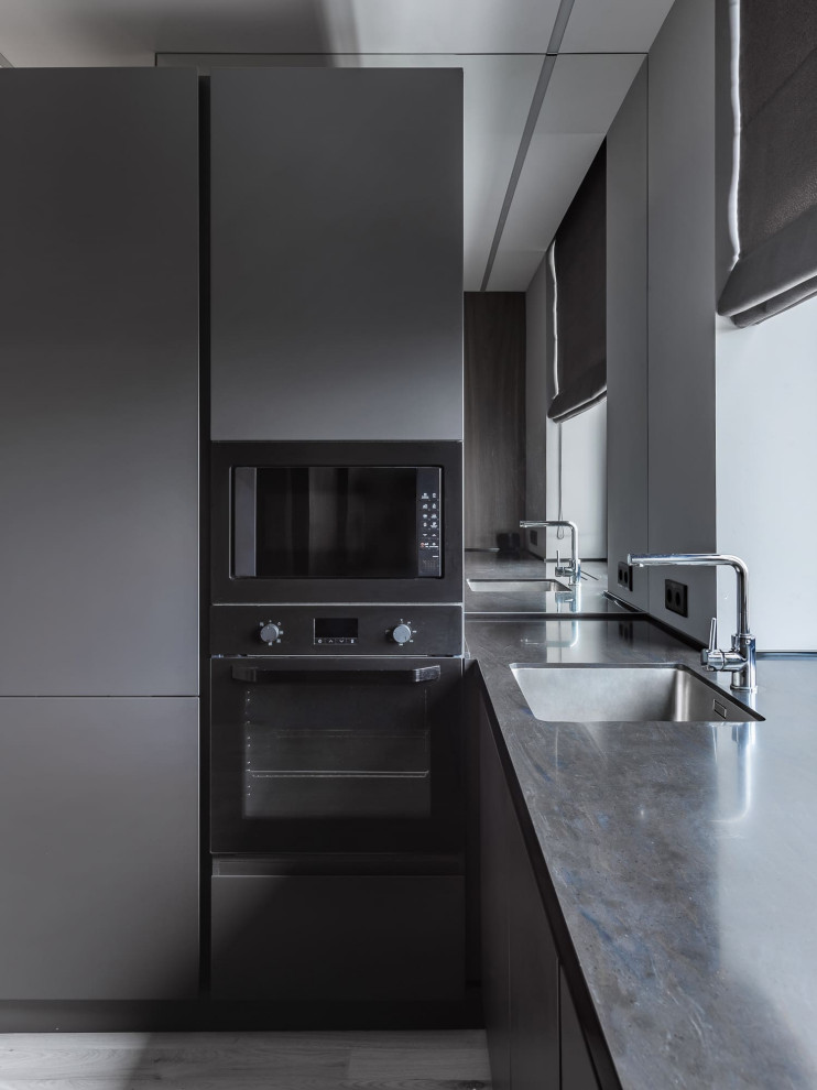 Diseño de cocina actual con fregadero bajoencimera, armarios con paneles lisos, puertas de armario grises y encimeras negras