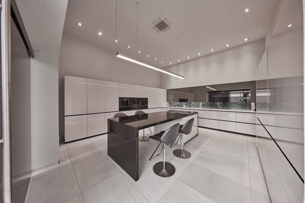 Стильный дизайн: отдельная, п-образная кухня в современном стиле с плоскими фасадами, белыми фасадами, черной техникой, островом и серым полом - последний тренд