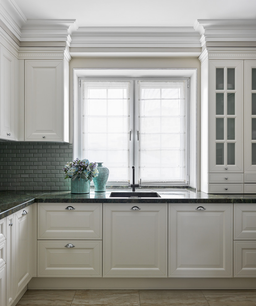 Klassisk inredning av ett avskilt, litet grön grönt l-kök, med en undermonterad diskho, luckor med infälld panel, beige skåp, granitbänkskiva, grönt stänkskydd, stänkskydd i porslinskakel, rostfria vitvaror, klinkergolv i porslin och brunt golv