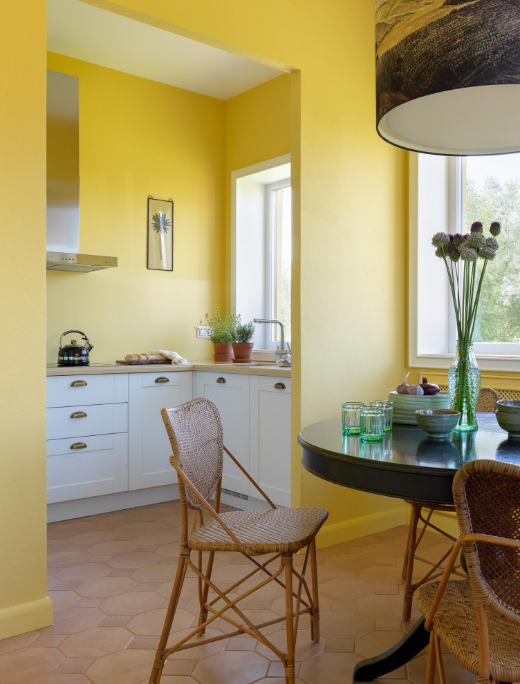 Aménagement d'une cuisine méditerranéenne en U avec un placard à porte shaker, des portes de placard blanches, une crédence jaune, un sol marron, un plan de travail beige et un évier encastré.