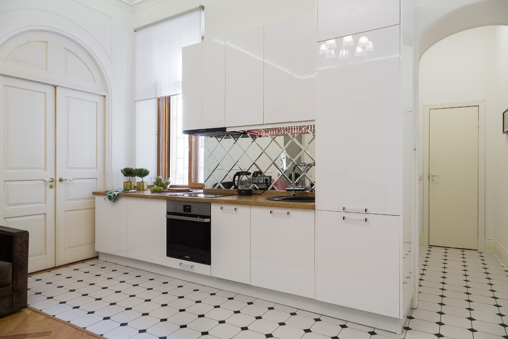 Inspiration för ett mellanstort linjärt kök med öppen planlösning, med en nedsänkt diskho, släta luckor, vita skåp, träbänkskiva, spegel som stänkskydd, rostfria vitvaror, cementgolv och vitt golv