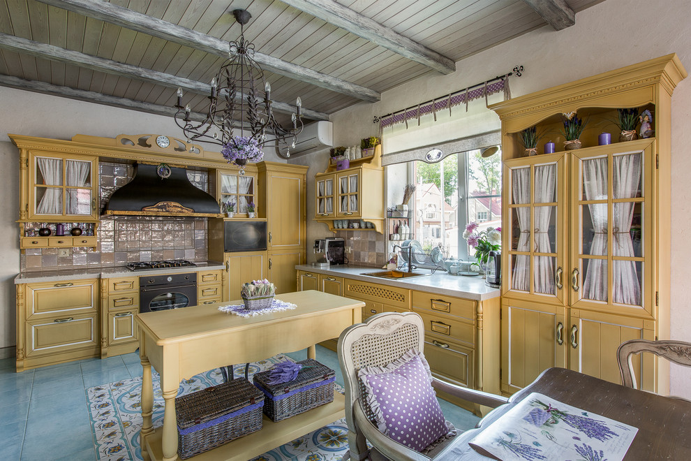 На фото: большая угловая кухня в классическом стиле с обеденным столом, накладной мойкой, фасадами с утопленной филенкой, желтыми фасадами, разноцветным фартуком, черной техникой, островом и бирюзовым полом с