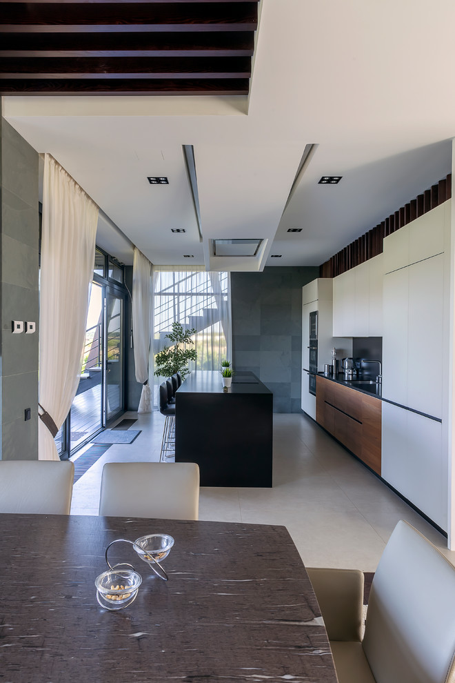 Свежая идея для дизайна: кухня-гостиная в современном стиле с монолитной мойкой, плоскими фасадами, белыми фасадами, черным фартуком и островом - отличное фото интерьера