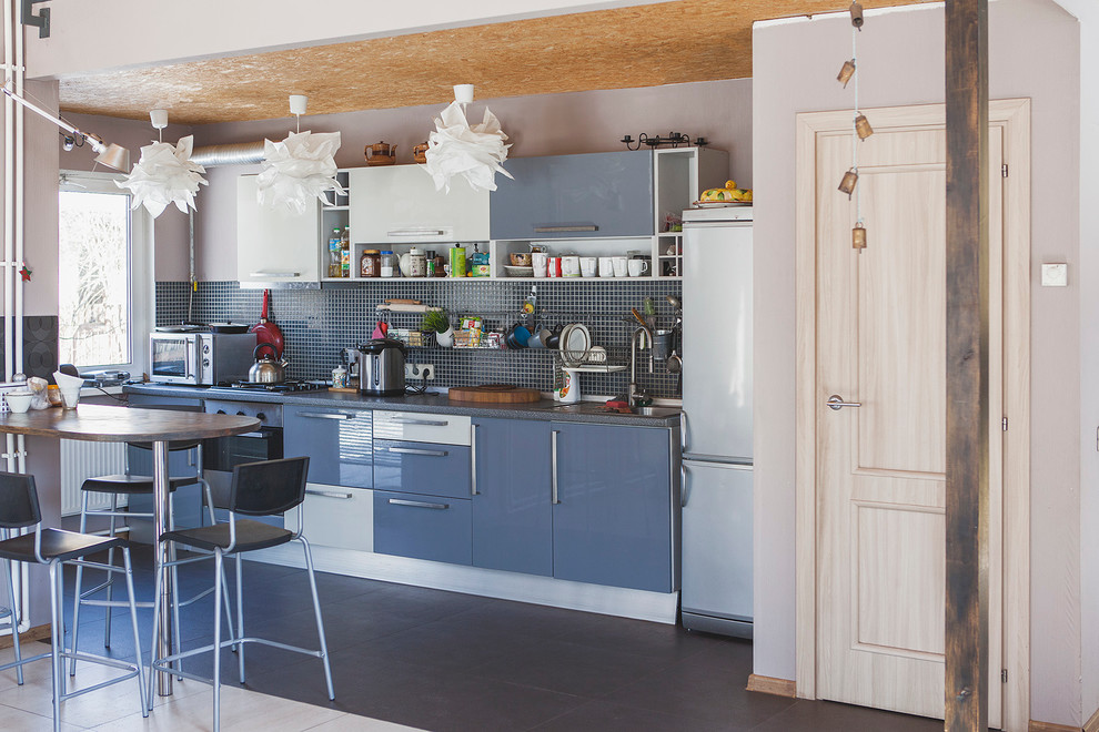 На фото: кухня в современном стиле с плоскими фасадами, синими фасадами и черным фартуком