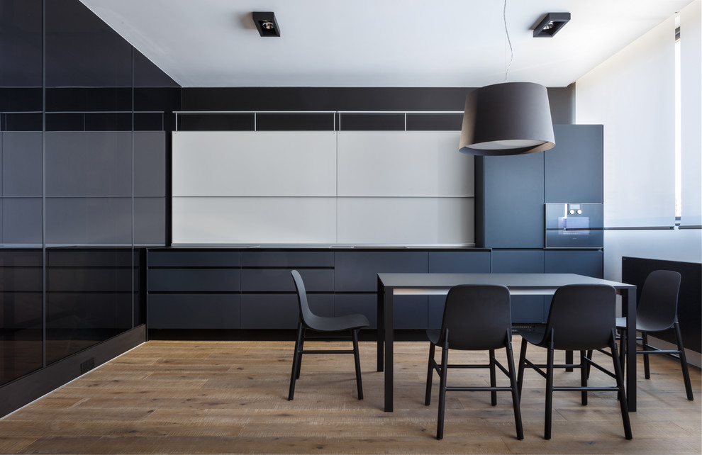 Foto di una cucina design con ante lisce, pavimento in legno massello medio, pavimento marrone, ante nere, paraspruzzi bianco, elettrodomestici neri e top nero
