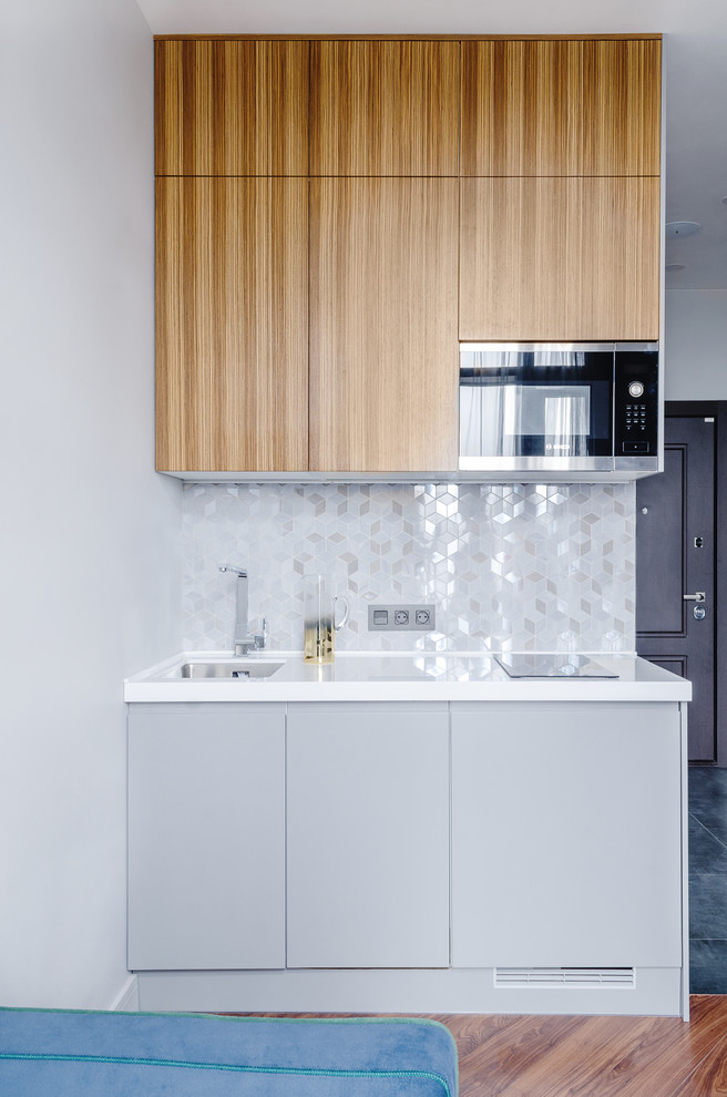 This is an example of a small contemporary single-wall kitchen/diner in Moscow with a submerged sink, flat-panel cabinets, medium wood cabinets, composite countertops, grey splashback, ceramic splashback, stainless steel appliances, laminate floors, brown floors and white worktops.