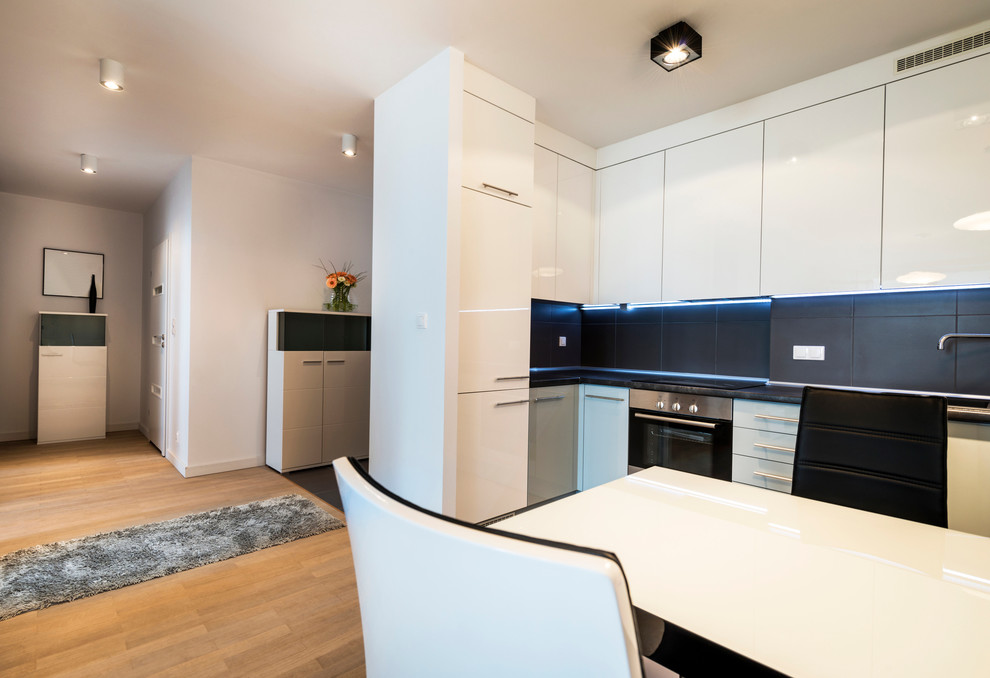 Photo of a medium sized scandi l-shaped open plan kitchen in Moscow with a built-in sink, flat-panel cabinets, white cabinets, laminate countertops, black splashback, ceramic splashback, stainless steel appliances, porcelain flooring and no island.