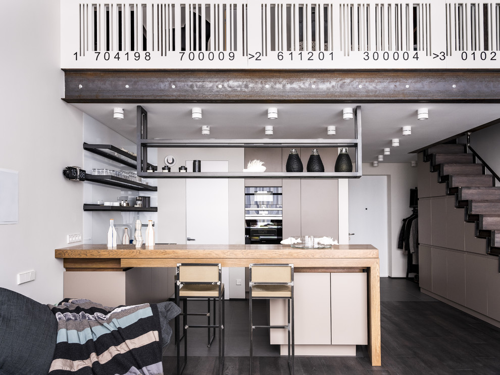 Свежая идея для дизайна: п-образная кухня-гостиная в современном стиле с плоскими фасадами, бежевыми фасадами, белым фартуком, черной техникой, полуостровом и черным полом - отличное фото интерьера