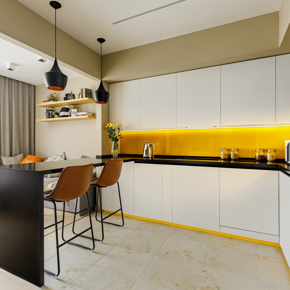 Пример оригинального дизайна: п-образная кухня среднего размера с обеденным столом, одинарной мойкой, белыми фасадами, столешницей из акрилового камня, желтым фартуком, фартуком из стекла, техникой под мебельный фасад и черной столешницей