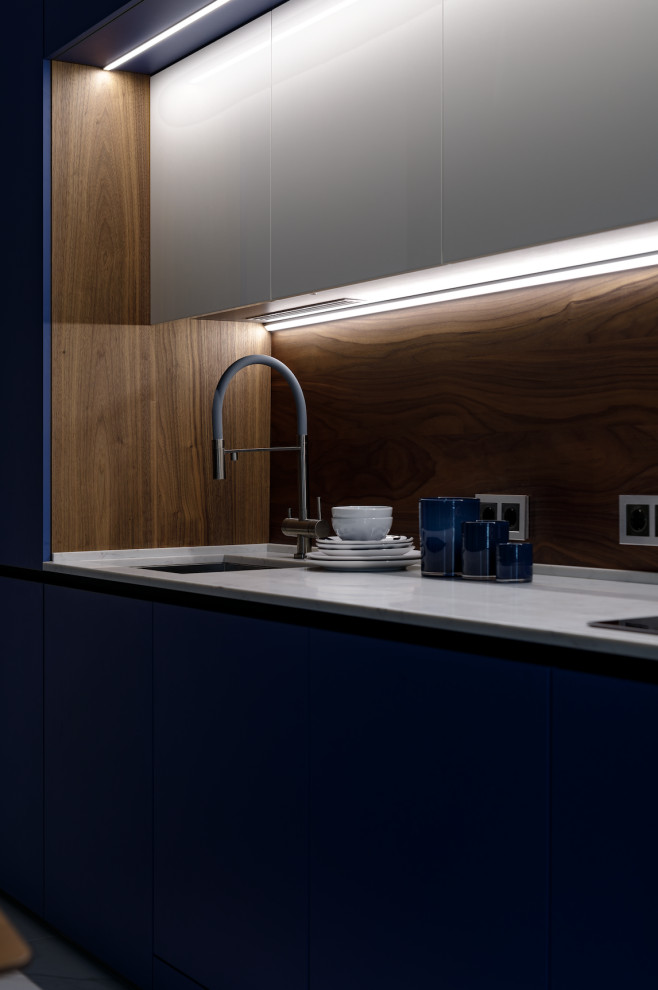 Modern inredning av ett mellanstort vit linjärt vitt kök och matrum, med en enkel diskho, blå skåp, bänkskiva i kvarts, brunt stänkskydd, stänkskydd i trä och integrerade vitvaror