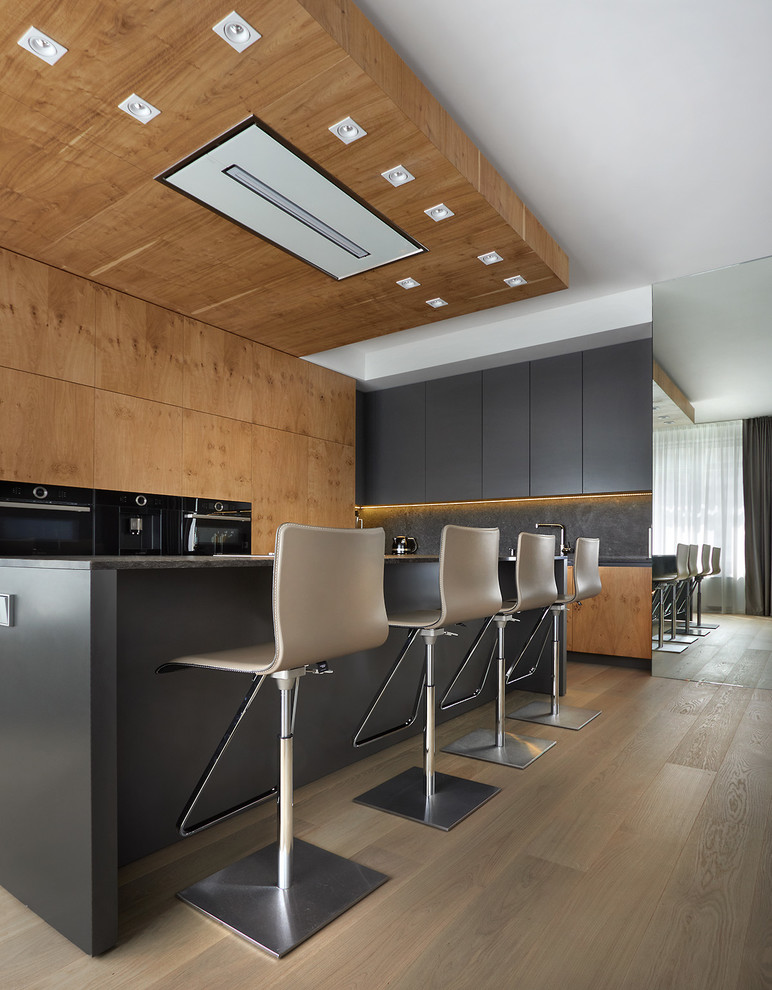 Esempio di una grande cucina design con ante lisce, paraspruzzi nero, elettrodomestici neri, parquet chiaro, pavimento beige, top nero e ante in legno scuro