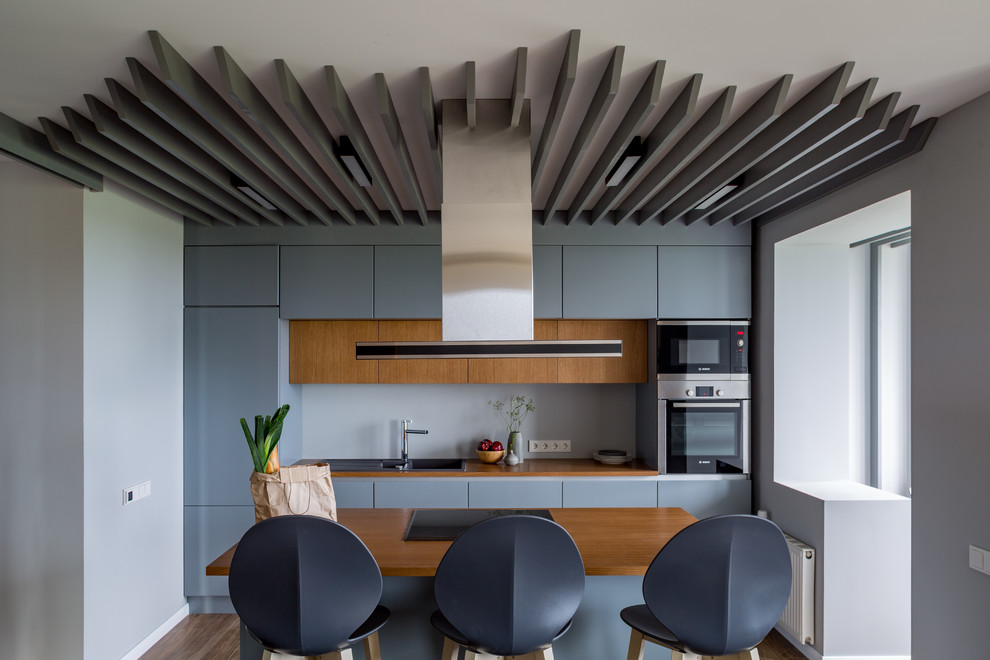 Идея дизайна: параллельная кухня среднего размера в современном стиле с обеденным столом, накладной мойкой, плоскими фасадами, синими фасадами, серым фартуком, техникой из нержавеющей стали и островом